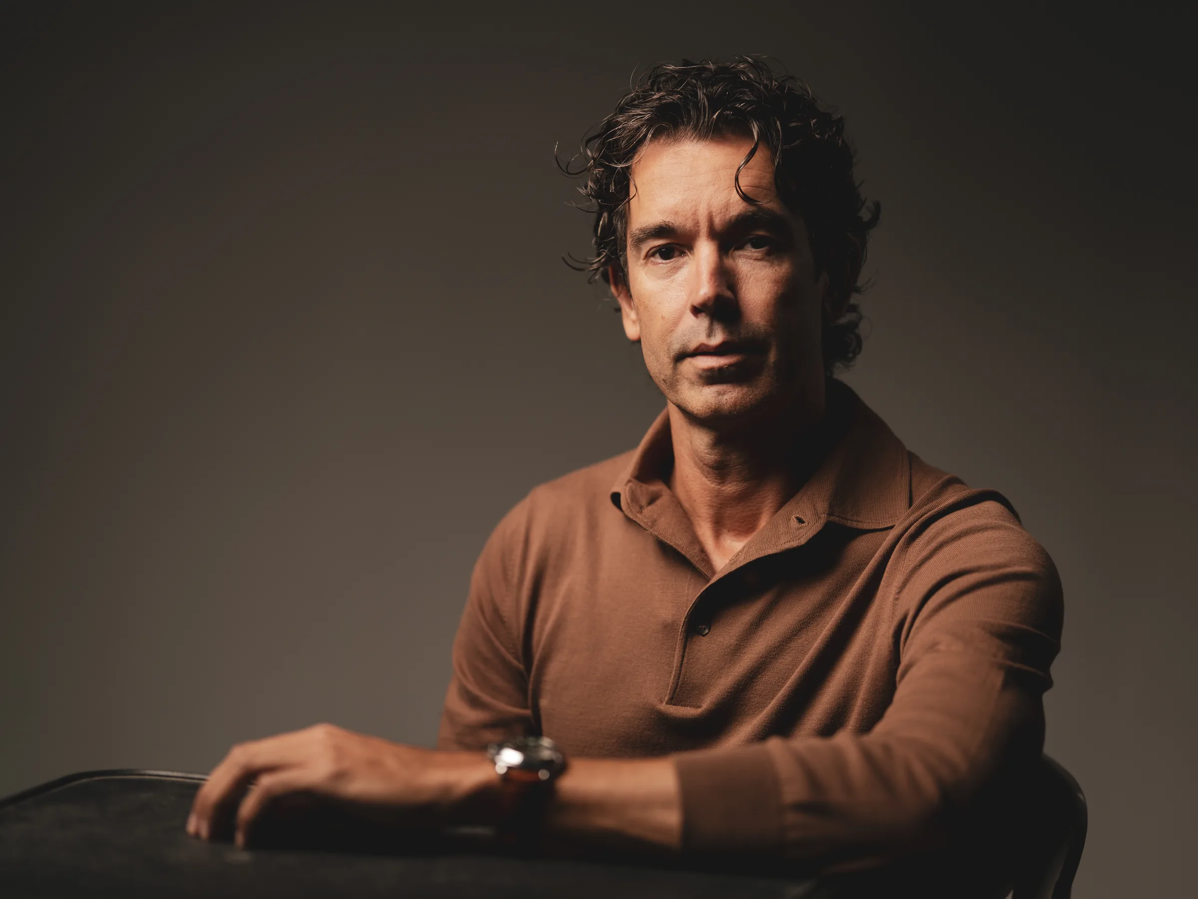 Studioportret van een man in bruine polo, leunend op een tafel
